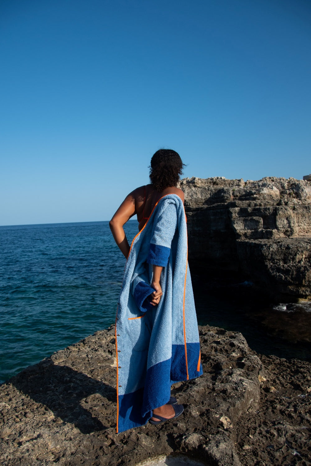 Model wearing Ramona blue long towelling robe with orange detail by the sea