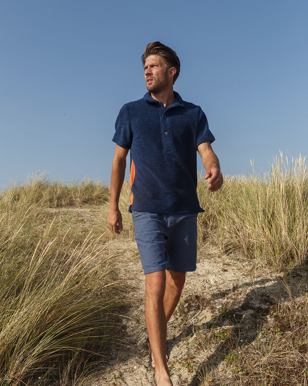 So English Bond polo shirt in navy and orange, featuring a casual fit and classic collar, worn by a model outdoors.