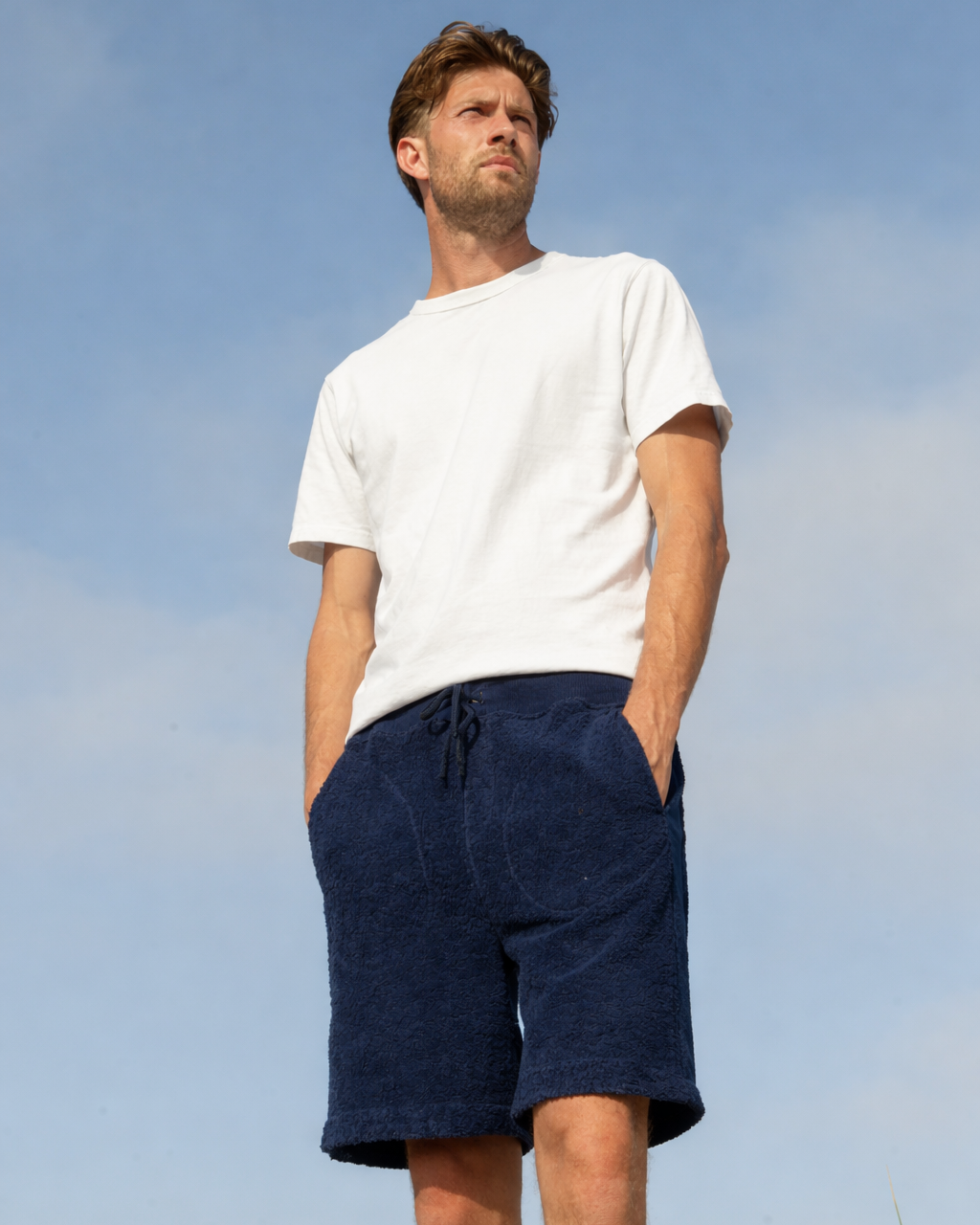 Male model wearing navy So English bear shorts in casual outdoor setting, showcasing relaxed beachwear style.
