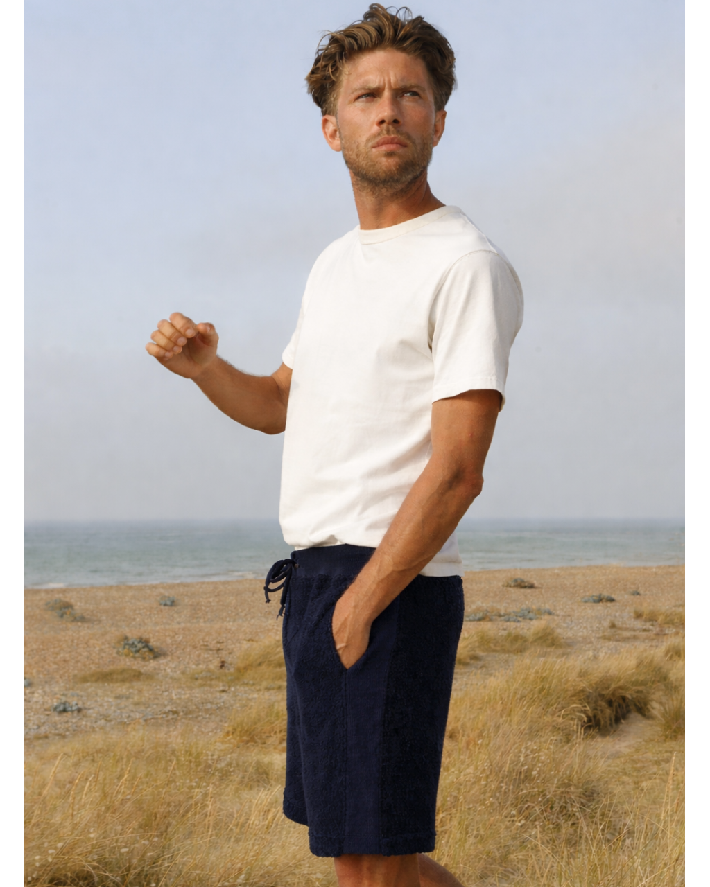 Man wearing navy Bear Shorts by So English on the beach, showcasing casual summer beachwear made in the UK.