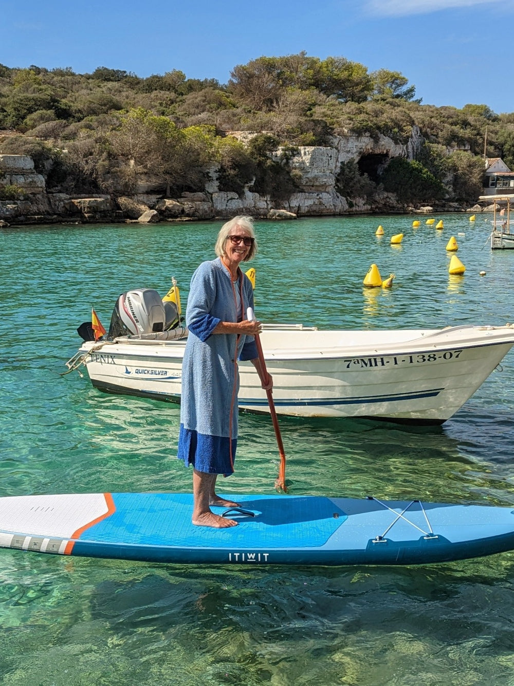 Older model wearing Ramona blue long towelling robe with orange detail on a paddle board