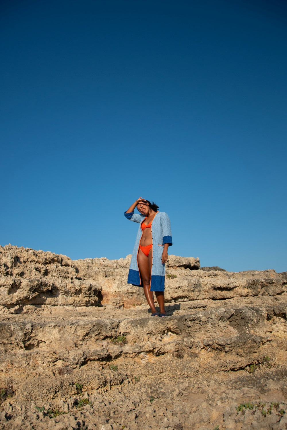 Model wearing Ramona blue long towelling robe with orange detail by the sea