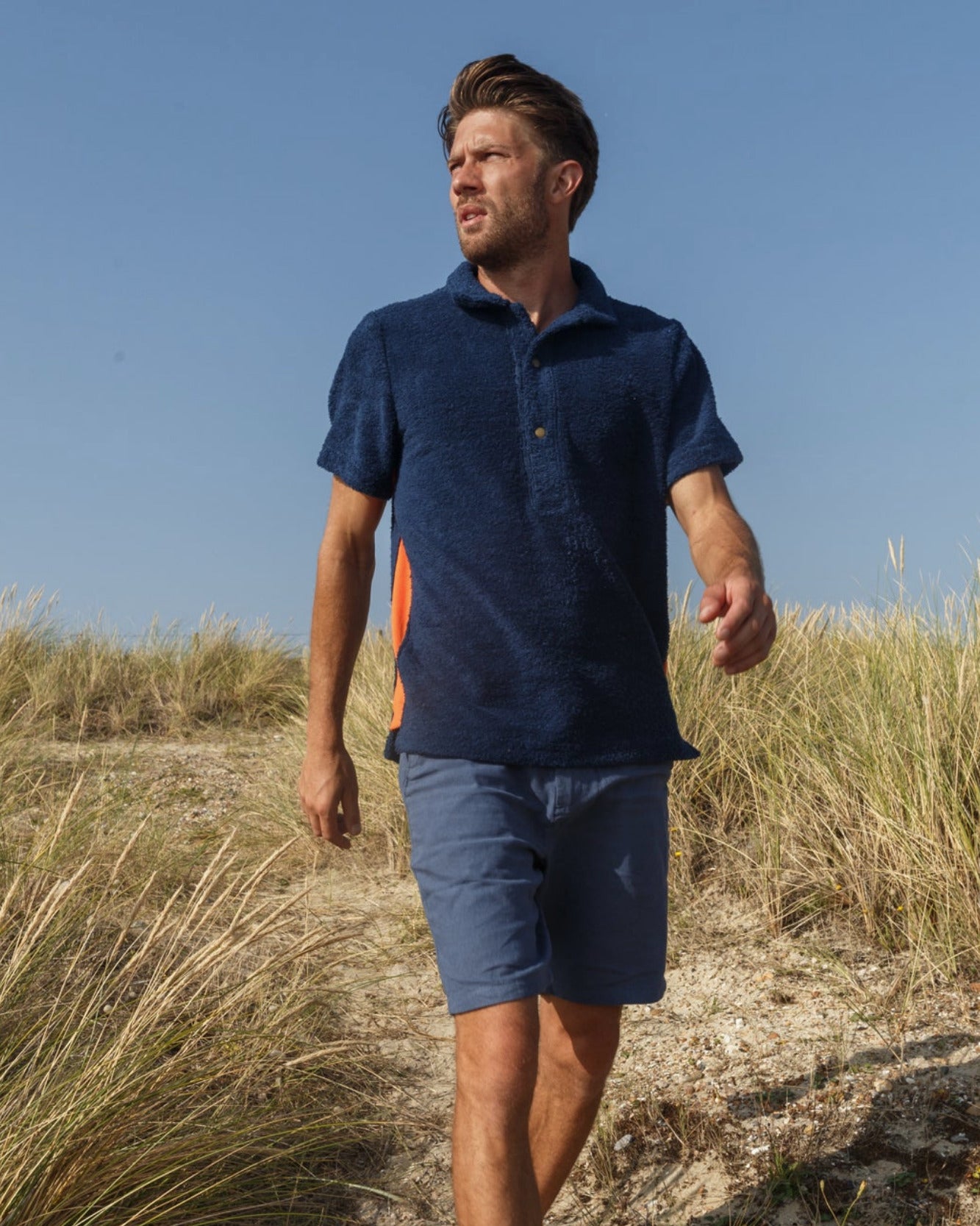 Navy and orange Bond polo shirt by So English, shown on a model in a casual beachwear setting, made in the UK.