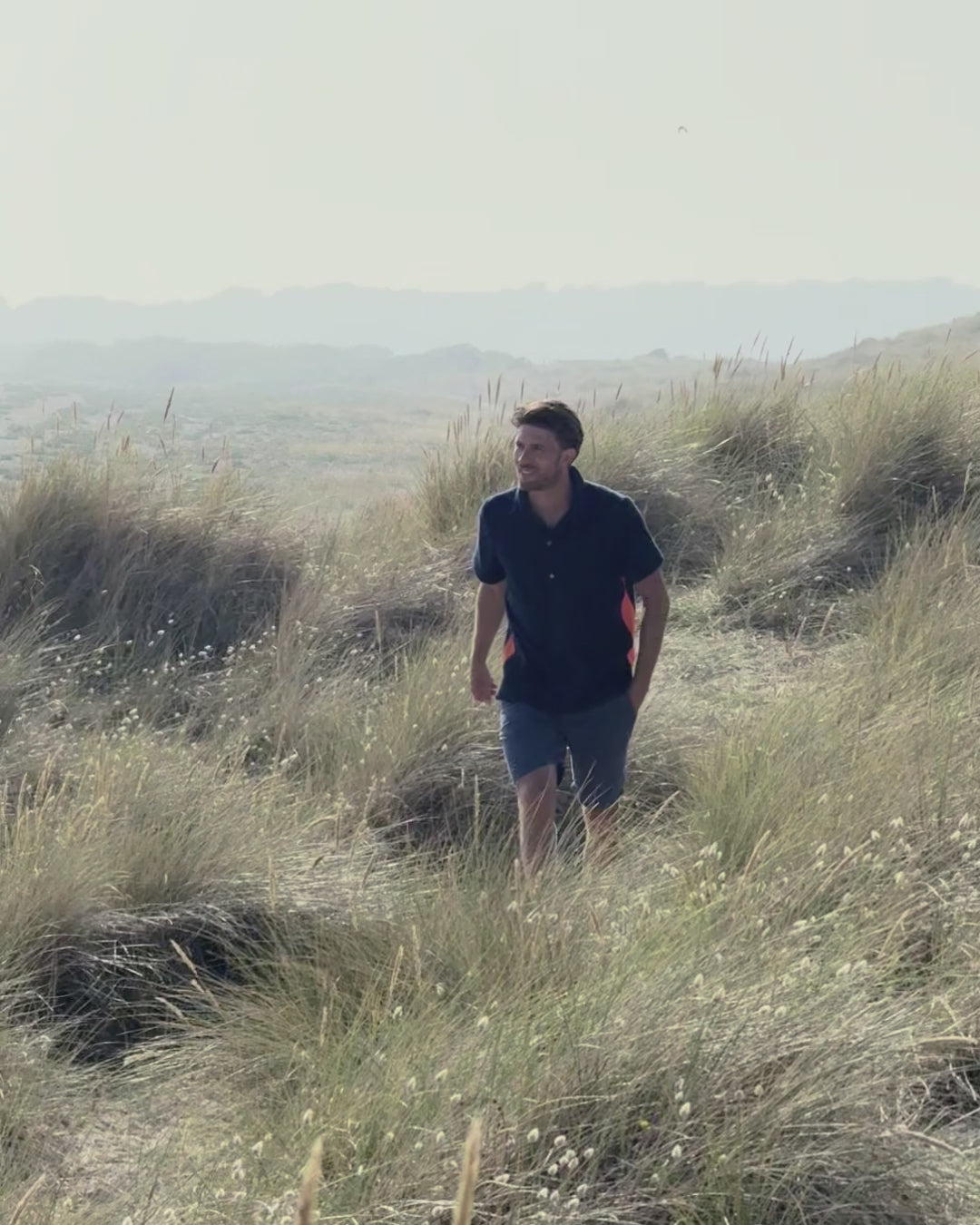 Video of a man walking through the dunes wearing the Bond terry towelling polo shirt in Navy by So English — Italian cotton, handmade in the UK.